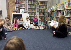 Dzieci siedzą na podłodze i słuchają opowiadania.