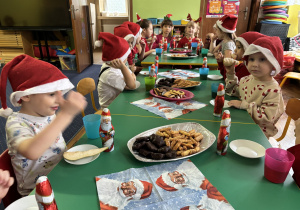 Dzieci siedzą przy stole i zjadają słodkości.