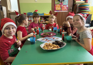 Dzieci siedzą przy stole i zjadają słodkości.