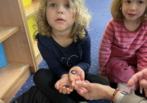 Dzieci siedzą w kole na dywanie i oglądają guziki.