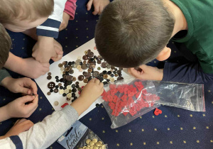 Dzieci siedzą w kole na dywanie i oglądają guziki.