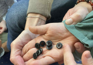 Dzieci siedzą w kole na dywanie i oglądają guziki.