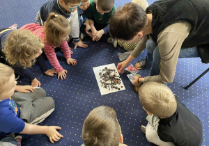 Dzieci siedzą w kole na dywanie i oglądają guziki.