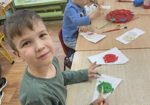 Dzieci siedzą przy stole i wykonują prace plastyczną.