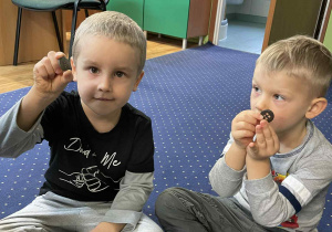 Dzieci siedzą w kole na dywanie i oglądają guziki.