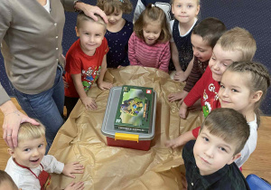 Dzieci siedzą przy stole i rozpakowują prezent od Mikołaja.