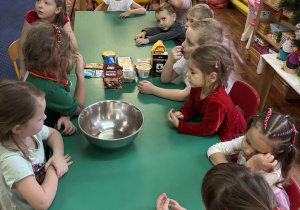 Dzieci siedzą przy stole na którym znajdują się produkty niezbędne do upieczenia pierniczków.