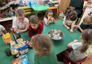 Dzieci siedzą przy stole na którym znajdują się produkty niezbędne do upieczenia pierniczków.