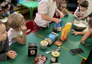 Dzieci siedzą przy stole, chłopiec odmierza cukier.