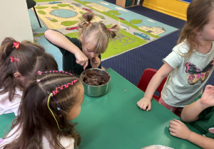 Dzieci siedzą przy stole, dziewczynka miesza produkty do rondelka.