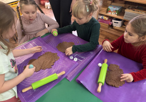 Dzieci siedzą przy stole, wałkują ciasto.