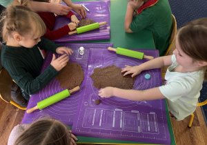 Dzieci siedzą przy stole, wałkują ciasto.