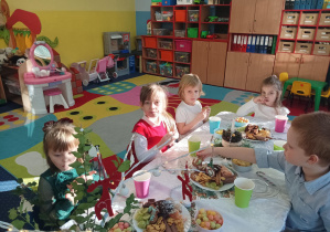 dzieci świętują wigilię klasową, siedzą przy stolikach, na których widać słodycze, owoce, soki