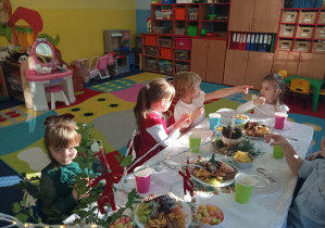 dzieci świętują wigilię klasową, siedzą przy stolikach, na których widać słodycze, owoce, soki