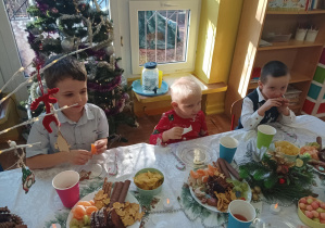 dzieci świętują wigilię klasową, siedzą przy stolikach, na których widać słodycze, owoce, soki