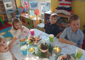 dzieci świętują wigilię klasową, siedzą przy stolikach, na których widać słodycze, owoce, soki