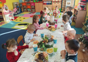 dzieci świętują wigilię klasową, siedzą przy stolikach, na których widać słodycze, owoce, soki