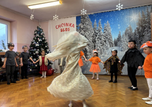 Dzieci ustawione w półkolu, królowa Lodu tańczy.