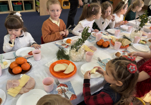 Dzieci siedzą przy stole i zjadają śniadanie.