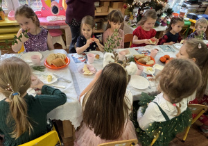 Dzieci siedzą przy stole i zjadają śniadanie.