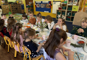 Dzieci siedzą przy stole i zjadają śniadanie.