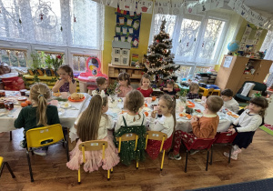 Dzieci siedzą przy stole i zjadają śniadanie.