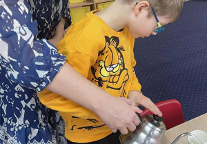 Chłopiec wraz z panią wlewa wodę do kubeczka.