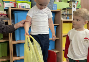 Chłopiec stoi na krześle podtrzymywany przez nauczyciela.