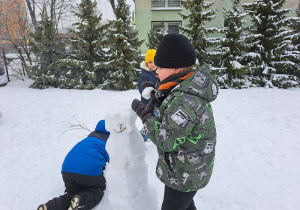 dzieci w ogródku lepią bałwana