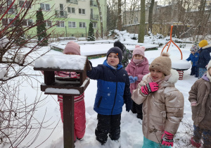 dzieci dokarmiają ptaki w ogródku przedszkolnym