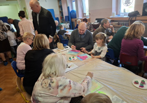 warsztaty plastyczne na sali gimnastycznej. dzieci razem z babciami i dziadkami wykonują ramki z lusterkami