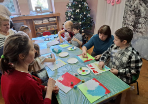 warsztaty plastyczne na sali gimnastycznej. dzieci razem z babciami i dziadkami wykonują ramki z lusterkami