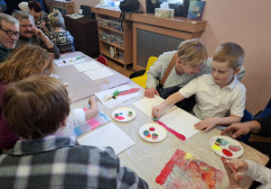 warsztaty plastyczne na sali gimnastycznej. dzieci razem z babciami i dziadkami wykonują ramki z lusterkami