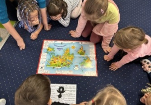 Dzieci siedzą w kole słuchając i obserwując mapę.