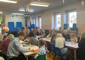 Dzieci wraz z dziadkami siedzą przy stołach i wykonują prezenty.