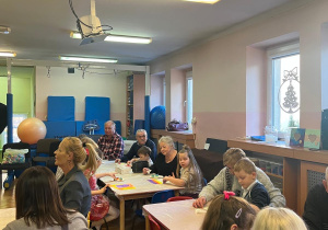 Dzieci wraz z dziadkami siedzą przy stołach i wykonują prezenty.