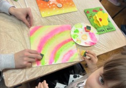 Dzieci wraz z dziadkami siedzą przy stołach i wykonują prezenty.