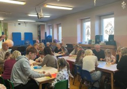 Dzieci wraz z dziadkami siedzą przy stołach i wykonują prezenty.