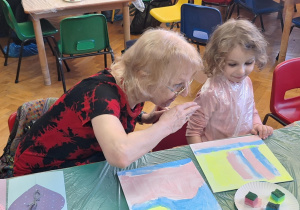 Dzieci wraz z dziadkami siedzą przy stołach i wykonują prezenty.