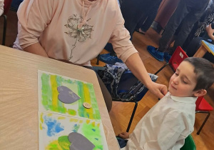 Dzieci wraz z dziadkami siedzą przy stołach i wykonują prezenty.