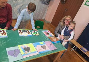 Dzieci wraz z dziadkami siedzą przy stołach i wykonują prezenty.