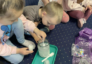 Dzieci siedzą na dywanie i wykonują doświadczenia ze śniegiem.