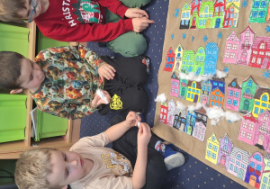 Dzieci siedzą na dywanie i wykonują zimową pracę plastyczną.