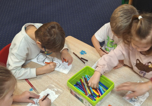 Dzieci siedzą przy stolikach i wykonują zadanie.