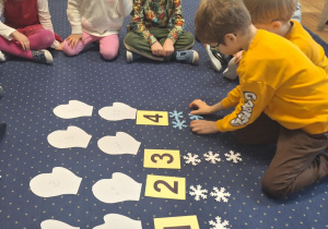 Dzieci siedzą na dywanie i przyporządkowują liczbę śnieżynek do cyfry.