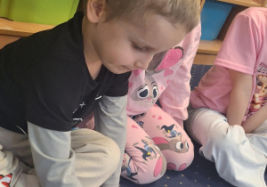 Chłopiec siedzi na dywanie i wiedzie palcem po cyfrze.