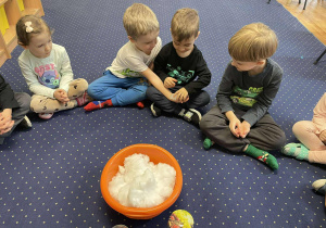 Dzieci siedzą na dywanie i doświadczają śniegu.