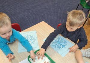 Dzieci siedzą przy stolikach i wykonują zadanie.