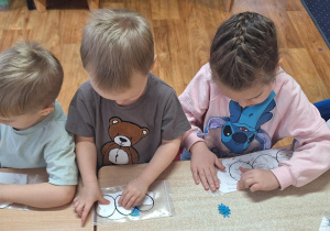 Dzieci siedzą przy stolikach i wykonują zadanie.