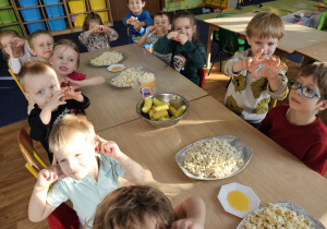 Dzieci siedzą przy stole na którym stoi popcorn.